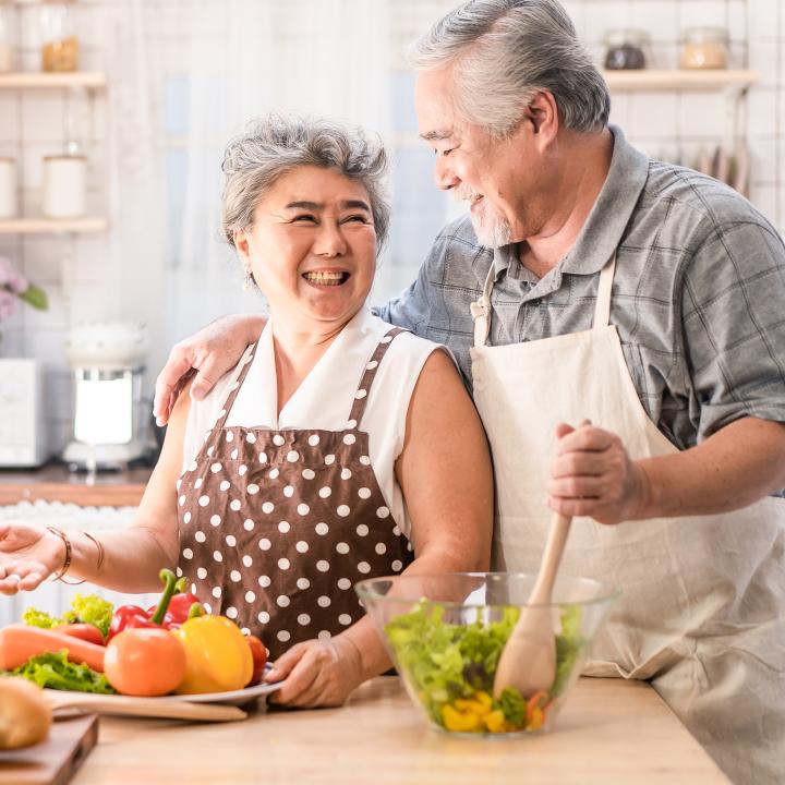 Happy senior couple preparing salad in kitchen