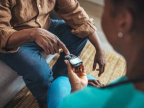 Elderly african american man with home health aide checking glucose