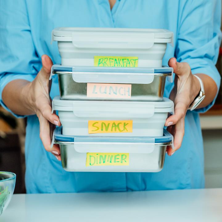 Woman holding labeled containers breakfast lunch snack dinner