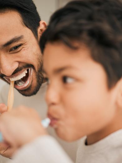 Happy Latino father and son brushing teeth together