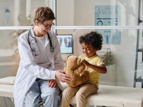 Female physician talking to a small boy who is holding a teddy bear