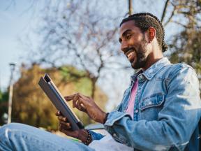 Young African American man on park bench looking at tablet computer screen