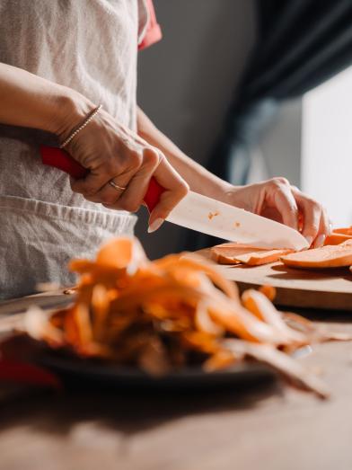 Young woman cutting sweet potato while cooking