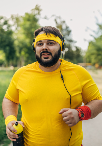 A stocky man wearing yellow exercise clothes is outside walking