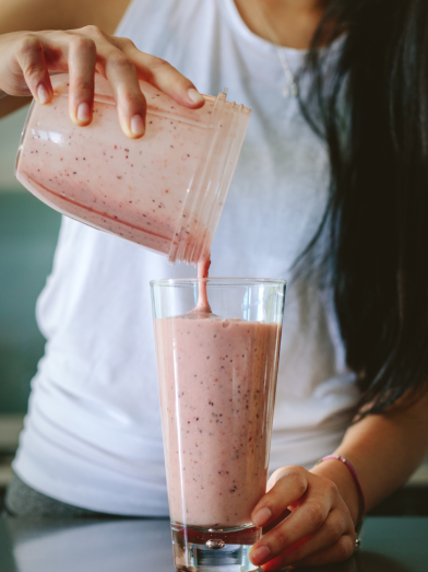 Two hands pour a pink smoothie into a glass.