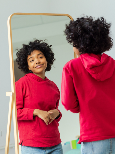 A younger woman looks in the mirror and smiles at herself. 