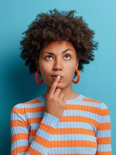 A woman looks quizzical with a finger on her mouth. 