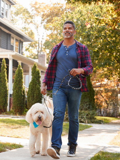 A Hispanic man walking his dog outside.