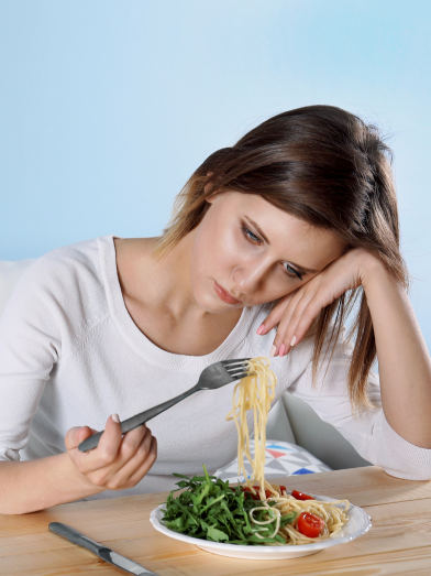 A sad woman stares at a plate of food. 