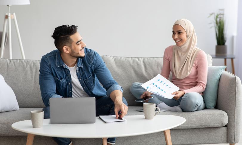 man and woman sitting on couch talking with laptop