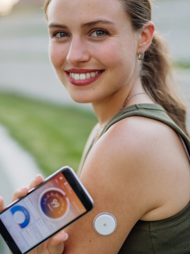 A woman in workout clothes holds her phone up to her CGM. 