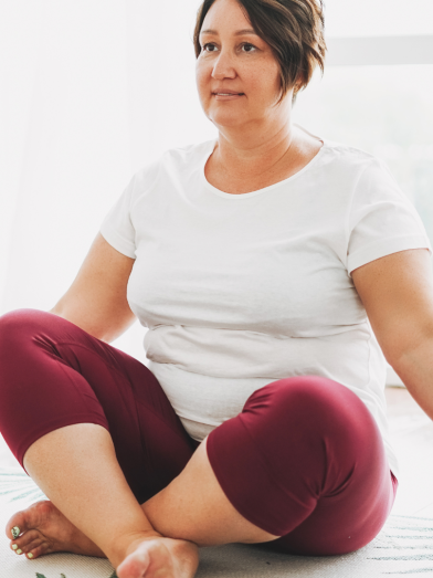 A woman sits on a yoga mat practicing a pose. 